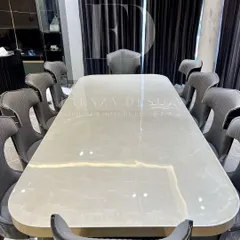 An opulent 10-seater dining set. The table features a lustrous white onyx top with a brass-trimmed base, surrounded by high-back chairs with unique cut-out details and dual-fabric upholstery.