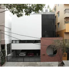 The Franklin Residence in Bengaluru presents a bold facade with a composition of white planes, red brick, and a black slatted screen. A circular opening in the brick wall creates a unique architectural signature and a playful focal point.