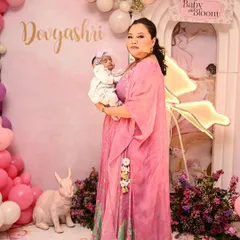 A mother and her newborn baby at a 'Baby in Bloom' celebration. The butterfly and floral backdrop in shades of pink and purple provides a beautiful setting for their first photos together.