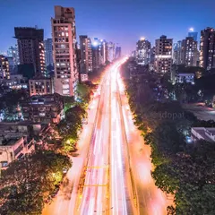A long-exposure photograph of a main road in Mumbai at night, where the light trails from traffic flow like a river of light through the city.