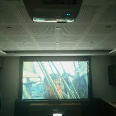 Here is a complete home theater system after a smooth and professional installation. The Epson projector is ceiling mounted, and the large fixed frame screen is flanked by powerful floor standing speakers and a dedicated AV console.