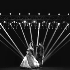 A couple's sangeet dance transformed into a work of art. The stark contrast of the spotlights against the dark stage creates a powerful and dramatic black and white image.