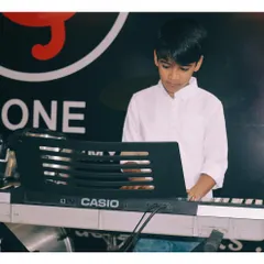 A young keyboard student practicing during a class. You can see his focus as he works on a piece, with the drums visible in the background, showing our multi-instrument environment.