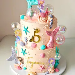 Dive into a magical underwater world with this two-tiered mermaid cake. Designed for a fifth birthday, it's decorated with pastel seashells, shimmering mermaid tails, and delicate bubble details, all crafted from whipped cream and fondant.