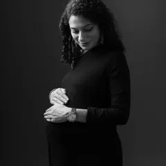 A quiet, contemplative moment captured in monochrome. This close-up portrait focuses on the mother's gentle expression as she looks down at her baby bump.