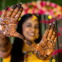 A creative shot of the bride showing off her stunning mehendi design. The focus on the hands with the bride's happy face blurred in the background is a popular and artistic pose.