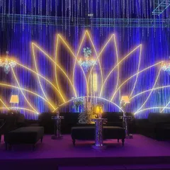 The main stage lounge area, set before a large neon lotus outline. The deep blue and purple lighting creates a moody, magical atmosphere perfect for an evening of music and dance.