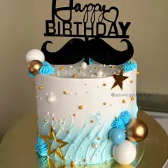 A stylish birthday cake for him, featuring a blue ombre wave design, a mustache topper, and gold and blue chocolate spheres.
