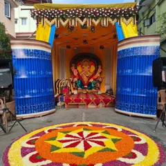 The complete outdoor setup for the Ganesh Chaturthi festival, including the decorated pandal, the large flower rangoli, and sound systems for the event.