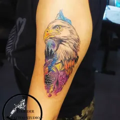 A vibrant, colorful eagle tattoo. This piece uses a watercolor and abstract style to incorporate a mountain landscape within the eagle's form, representing freedom and strength.