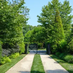 A creative driveway design using a combination of gravel and twin strips of turf. This approach softens the hardscape and is framed by lush, layered plantings and mature trees for a grand entrance.