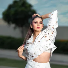 A high-fashion outdoor portrait for a magazine. The pose and high ponytail hairstyle complement the structured, modern design of the white laser-cut outfit.