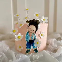This cake features a hand-painted character using cocoa butter, surrounded by delicate wafer paper daisies. It's a beautiful example of how I combine different edible mediums to create a unique artistic style.