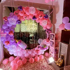 A grand 'Welcome Baby' decoration for a home entrance. This setup includes a crescent-shaped balloon arch in pink, purple, and lavender, a 'Welcome Baby' neon sign, and the floor decorated with rose petals spelling 'WELCOME'.