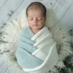 A beautifully swaddled newborn in a two-toned wrap, resting on a soft fur rug. This top-down angle is a classic way to show off the baby's peaceful state and perfect form.