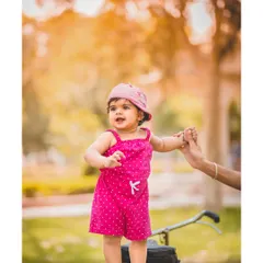 An outdoor first birthday shoot is a wonderful way to capture a baby's new mobility. Here, a little girl in a bright pink outfit stands proudly on a tricycle, holding her parent's hand for support in a beautiful, natural setting.