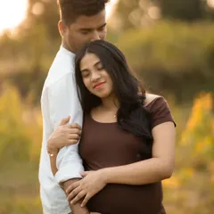 An intimate moment between an expecting couple, captured outdoors during golden hour. The warm light creates a romantic and gentle mood.