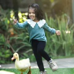 Pure joy in the garden. A little girl shares a playful moment with a duckling, a perfect example of the spontaneous fun we can capture outdoors.