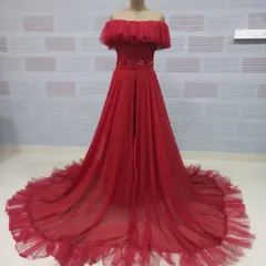 A full view of the red off-the-shoulder gown, revealing its long, flowing skirt and ruffled hem. The design provides a flattering silhouette while adding a touch of romantic drama.