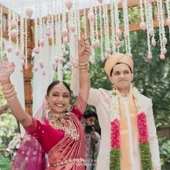 A triumphant moment as the newly married couple raises their hands in celebration under a beautiful floral mandap.
