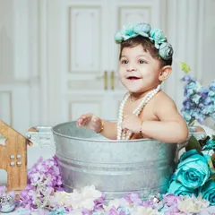 A joyful baby enjoying a milk bath session. The setup is adorned with blue and purple flowers for a beautiful, soft look.
