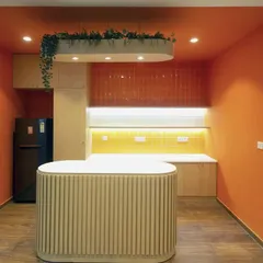 A modern pantry space featuring a fluted island counter and warm, recessed lighting against orange and yellow tiled backsplashes. This compact yet stylish area provides all necessary amenities for a quick coffee break.