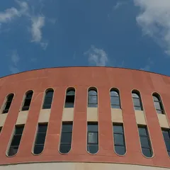 The curved red sandstone facade of the Mount Carmel School against the sky. This element adds warmth and texture to the building's circular form, with arched windows creating a rhythmic pattern that defines the upper levels.