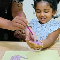 A teacher helps a smiling child with a hand printing craft. These one-on-one moments are key to our nurturing approach.