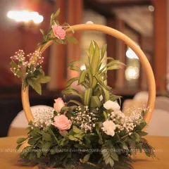 A modern and artistic floral centerpiece. This design features a golden circular frame adorned with soft pink roses, white carnations, and delicate baby's breath.