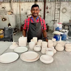 A proud student with his collection of bisque-fired work. He has created a full set of plates, bowls, and cups, all ready for the exciting glazing stage.