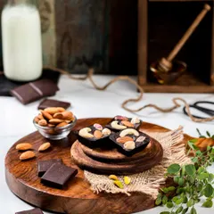 This image of nut-filled dark chocolates uses a rustic wooden setup to convey a handmade, artisanal quality. The scattered almonds and natural textures create a warm and inviting scene for a confectionery brand.