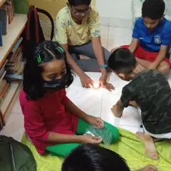 A group of students gathered on the floor, completely absorbed in an experiment with light. This is what focused, curiosity-driven learning looks like.