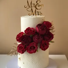 A classic two-tiered wedding cake with deep red roses and a "Mr & Mrs" topper. The textured bottom tier adds a modern touch.