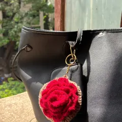 This is my crochet rose earphone case, shown here attached to a black bag. The vibrant red rose really stands out and adds a romantic touch to your accessories.