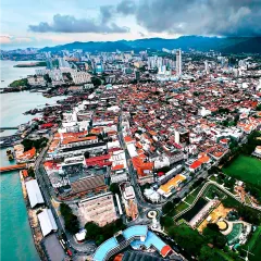 A wide aerial photograph of George Town, Penang, a UNESCO World Heritage Site. This shot captures the beautiful coastline and the dense, historic urban fabric of the city, taken during a project with AirAsia.