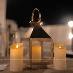 A close-up of a rustic yet elegant table setting. A brass lantern and flameless pillar candles create a warm, intimate, and safe ambiance for evening events.