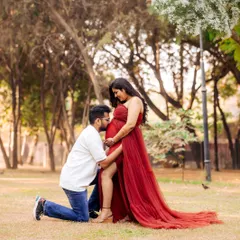 An intimate moment captured in a park setting. The partner kneels to embrace the baby bump, surrounded by the warm glow of the sun, creating a deeply romantic pregnancy photo.
