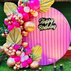 A close-up of a vibrant and trendy birthday backdrop. I used a circular pink panel with a custom "Happy Birthday" neon sign, accented with hot pink and chrome gold balloons and dried palm leaves for a modern look.