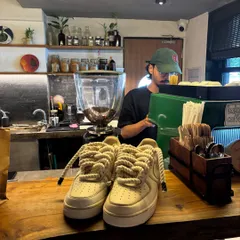 The coffee-themed custom sneakers sitting on a cafe counter, with a barista in the background.