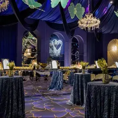 The bar area for the blue cocktail event, set against a backdrop of elegant arches and a neon sign of two swans. The mirrored bar front reflects the deep colors and lights of the room.