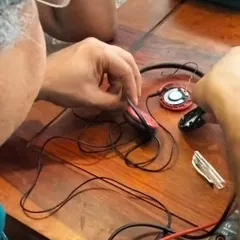 A close up of a mentor's hands carefully repairing a set of headphones. This image highlights the precision and patience required for delicate electronic repairs.