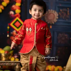 A handsome little boy dressed in a traditional sherwani and dhoti for a festive shoot. His happy expression and the vibrant, celebratory background make for a perfect portrait.
