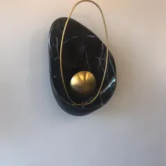 A detailed view of the 'Bird Nest' wall lamp. This piece showcases the beautiful contrast between the organic, polished black marble and the delicate, ring-shaped brass element that encircles the light source.