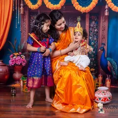 A heartwarming family portrait with a Krishna theme. Mom and big sister look on lovingly as the youngest is dressed as little Krishna, creating a beautiful memory for the whole family.