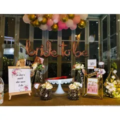 A full view of a stylish bachelorette party dessert table. The setup includes 'Bride to be' foil balloons, fun signage, and a pink and gold balloon garland for a festive, celebratory look.