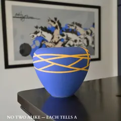 No two are alike, each tells a story of craft and culture. This stunning blue and yellow vase is placed on a console, demonstrating how a single, vibrant decor piece can complement and elevate the art behind it. The colors create a harmonious dialogue between object and artwork.