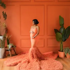 A bold and vibrant solo portrait. The rich orange tones and dramatic gown create a powerful image of a fierce mama-to-be.