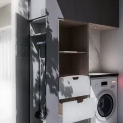 A smart and compact laundry area design, featuring a dedicated nook for the washing machine and a pull-out cabinet for storing cleaning supplies neatly.