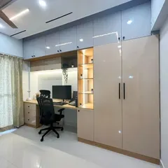A complete and functional home office setup. This design integrates a spacious desk, overhead cabinets, and a full-sized wardrobe, creating a seamless and organized workspace within a bedroom.