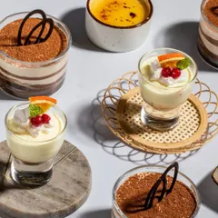 An artful arrangement of our dessert offerings. The vibrant colors of the Vanilla Mascarpone Bliss with Berries contrast beautifully with the rich cocoa of the Tiramisu, showcasing the visual appeal of our sweet treats.